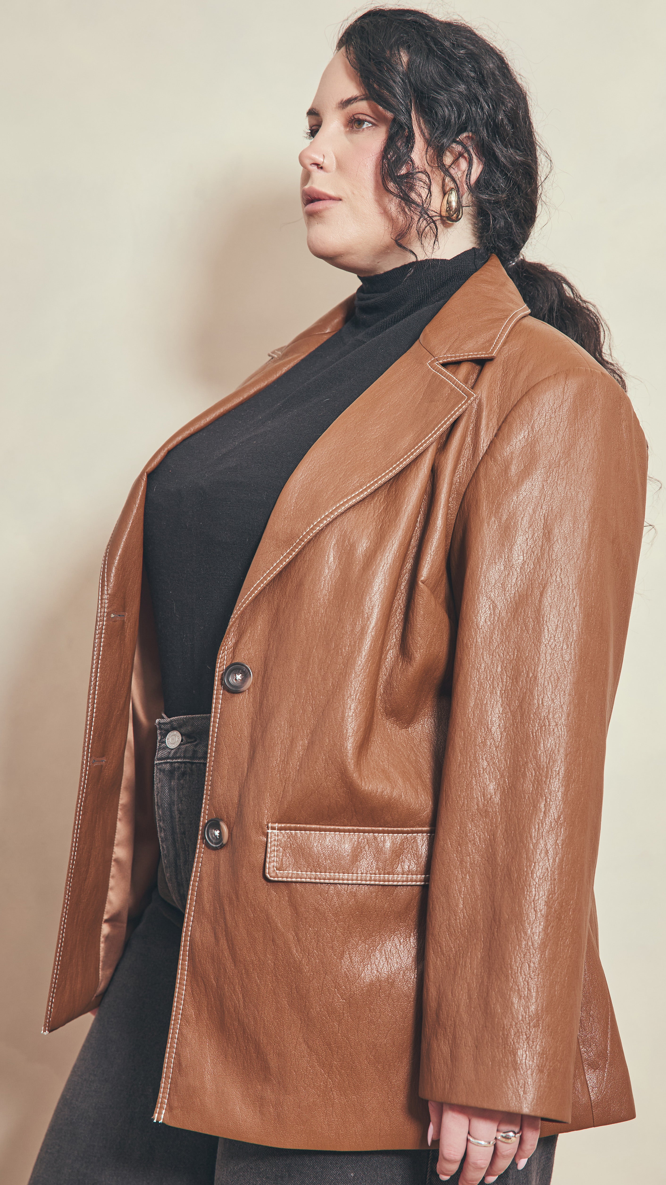 Side front view of model wearing a burnt toffee jacket showing welt pocket detail and all contrast cream stitching