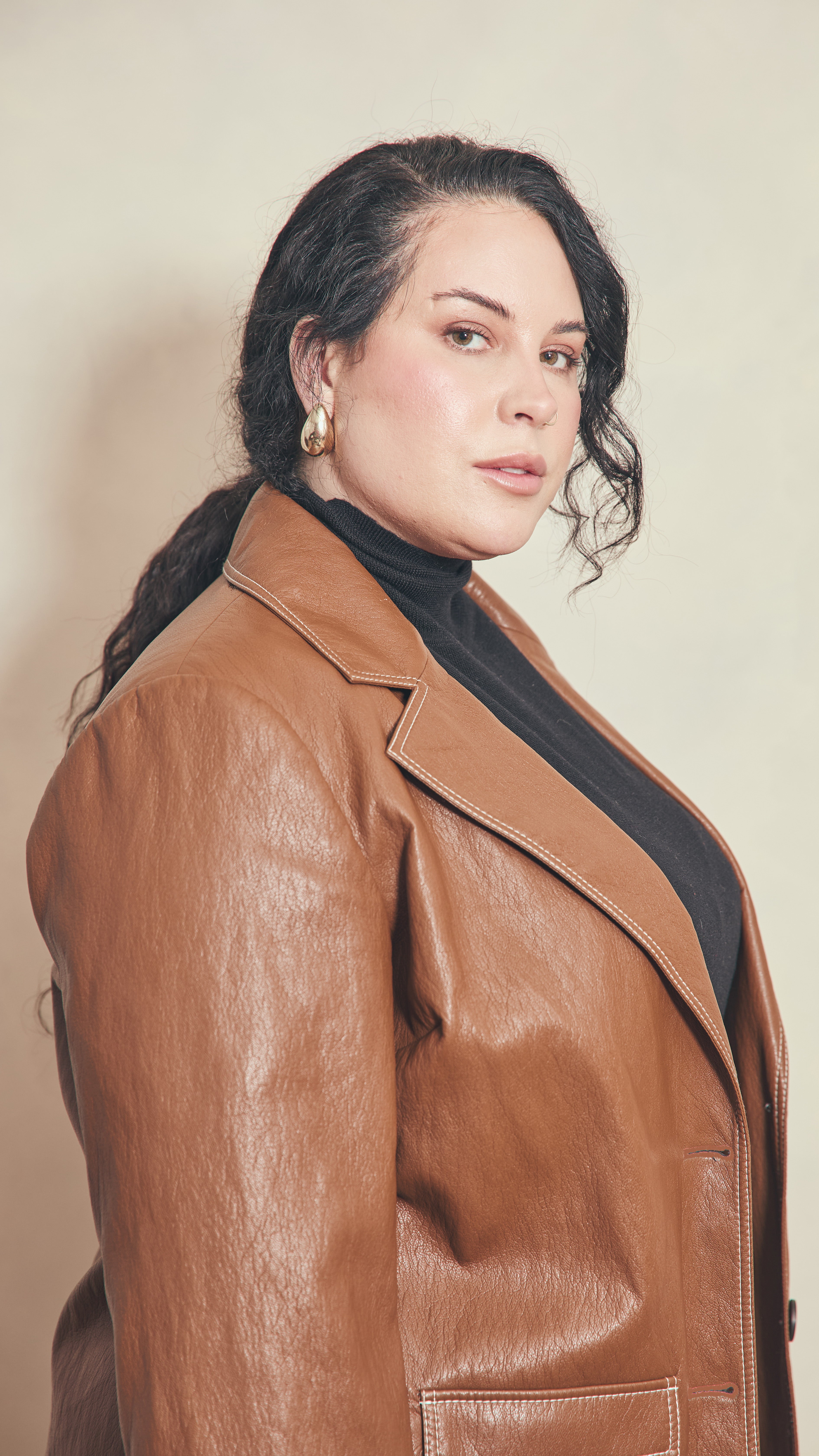 Modal wearing a burnt toffee jacket showing revere collar and lapel with contrast stitching, standing against a plain background