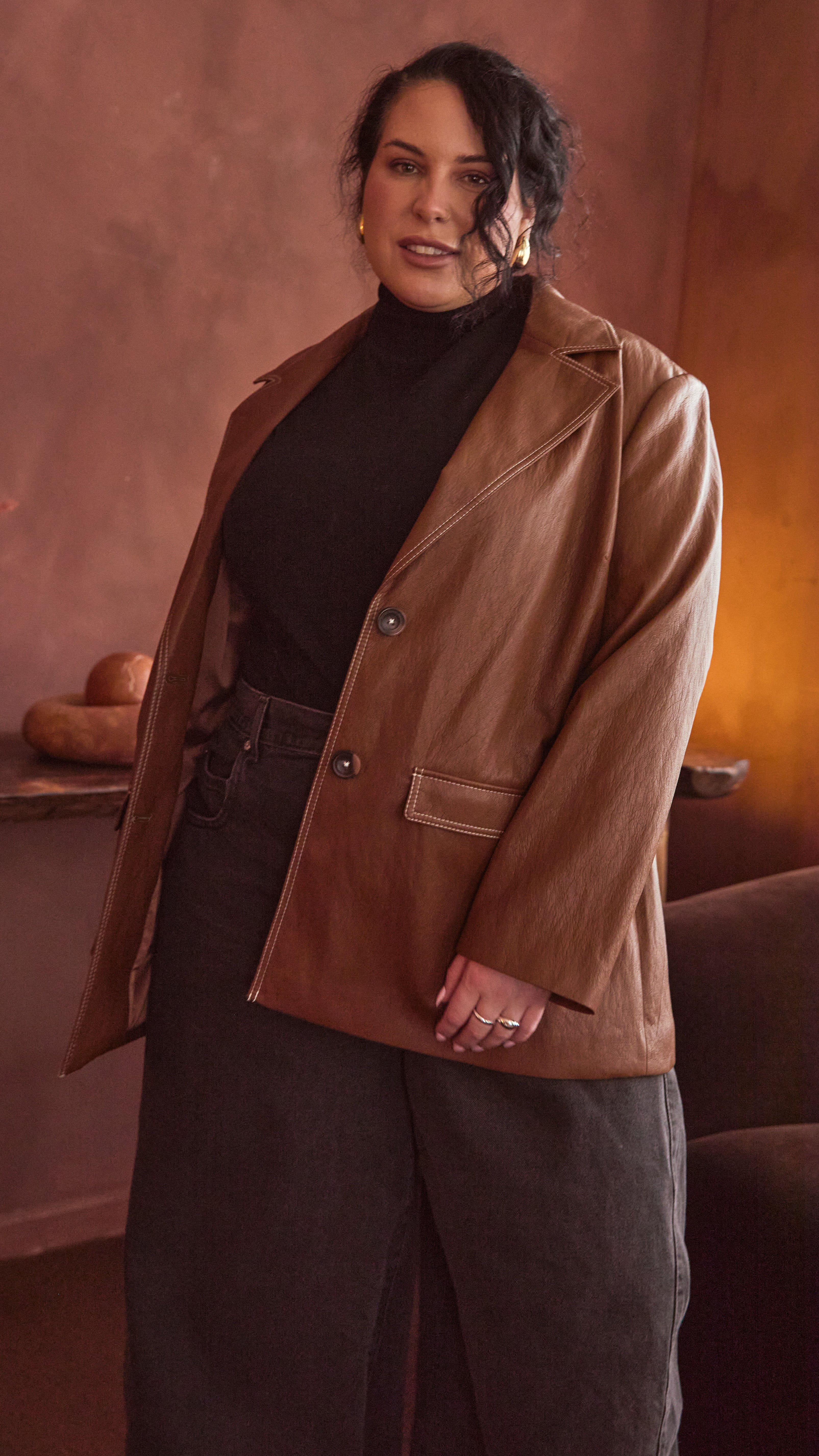 Modal wearing a burnt toffee blazer with a black turtle neck & black denim barrel leg jeans, in a warm-toned room