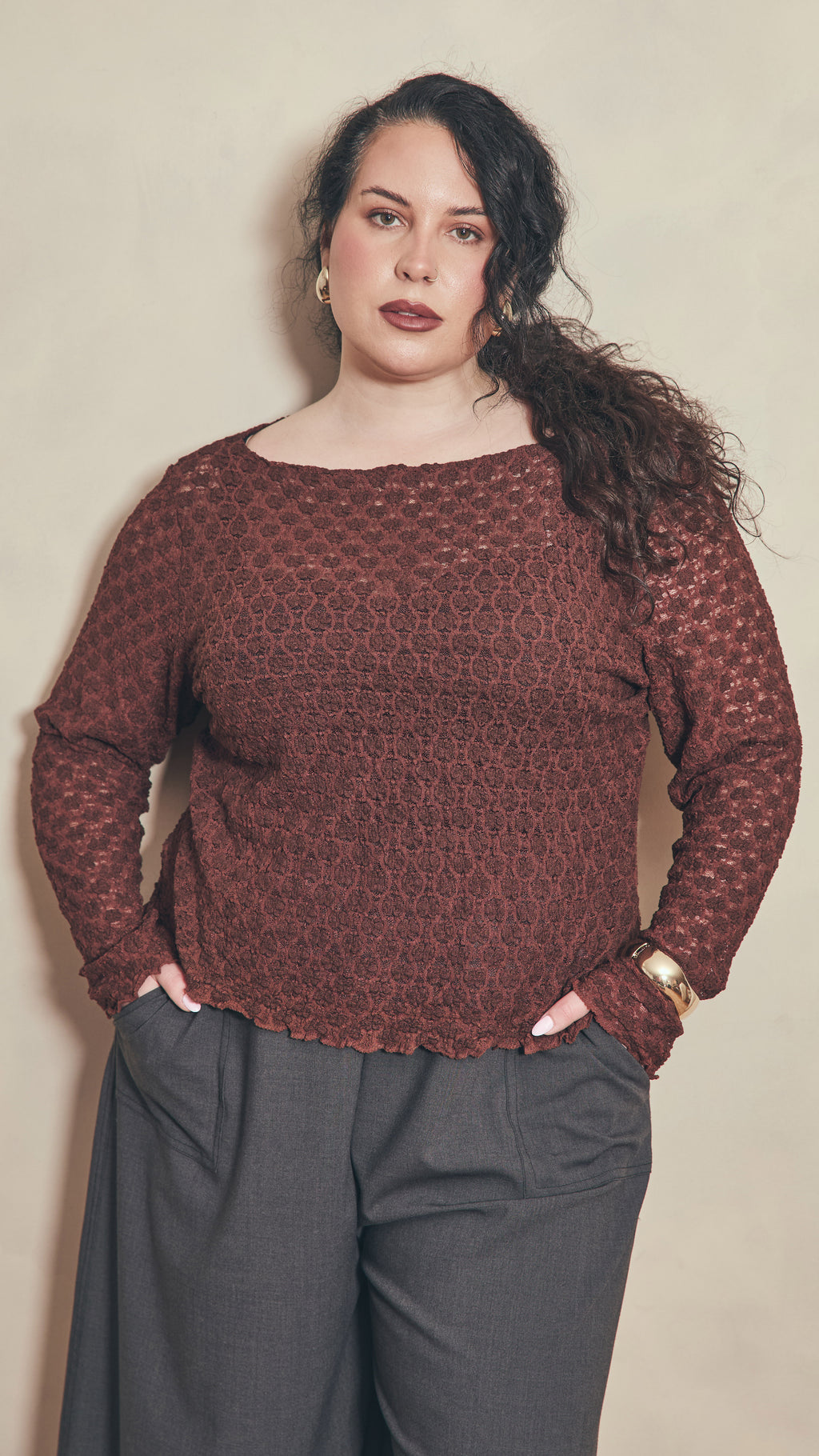 Modal leaning against plain colour wall wearing a chocolate lace top.