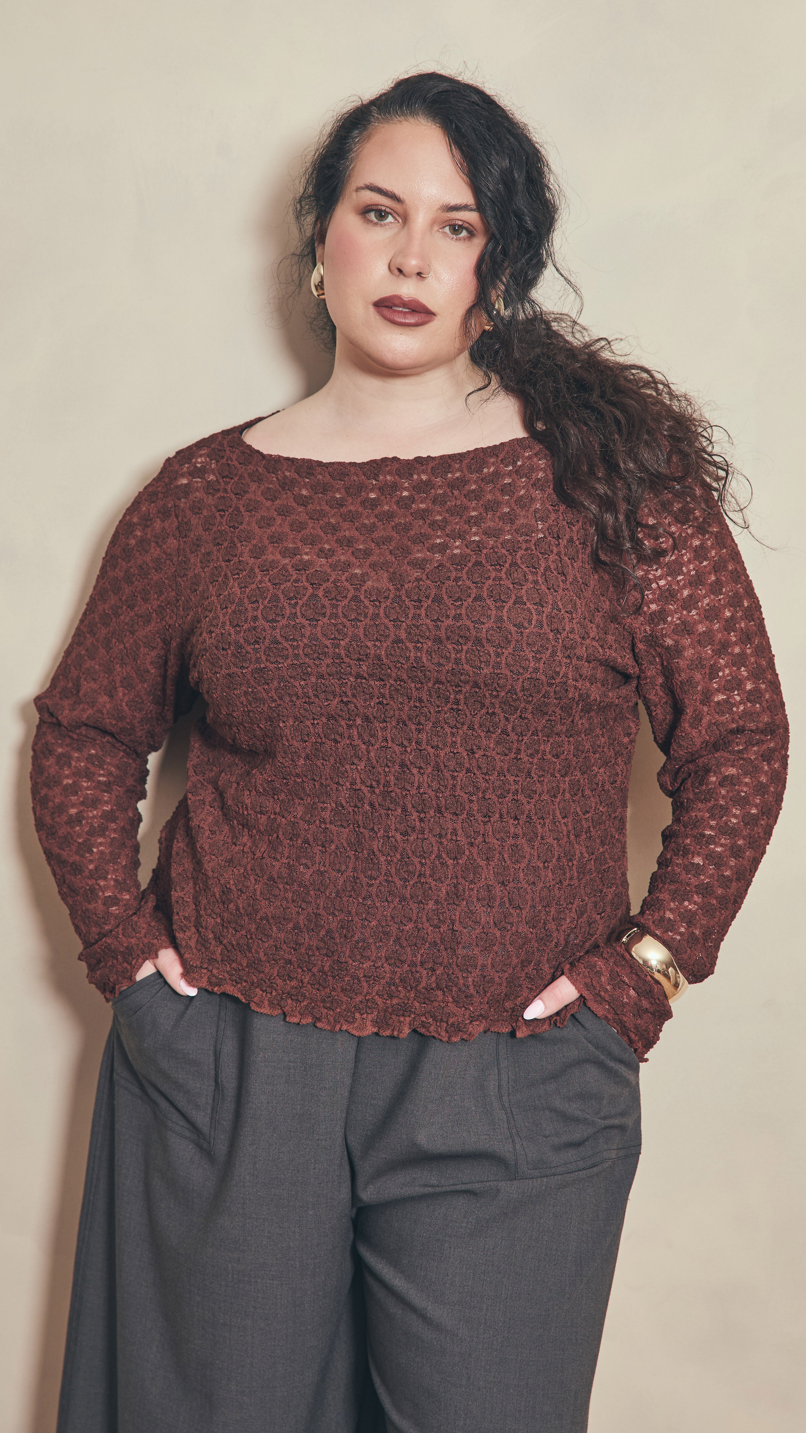 Modal leaning against plain colour wall wearing a chocolate lace top.