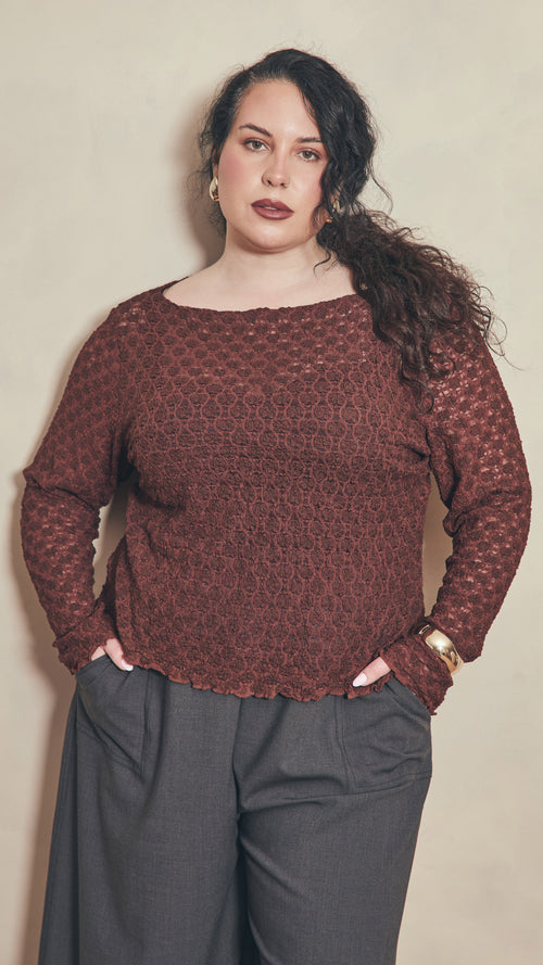 Modal leaning against plain colour wall wearing a chocolate lace top.